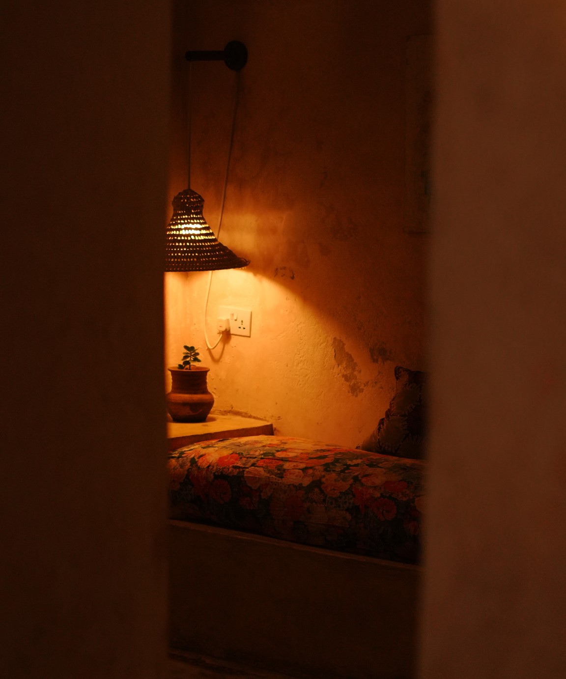 Firefly Boutique Hotel — a bedroom glimpsed through a doorway, woven lamp lit above a floral bed