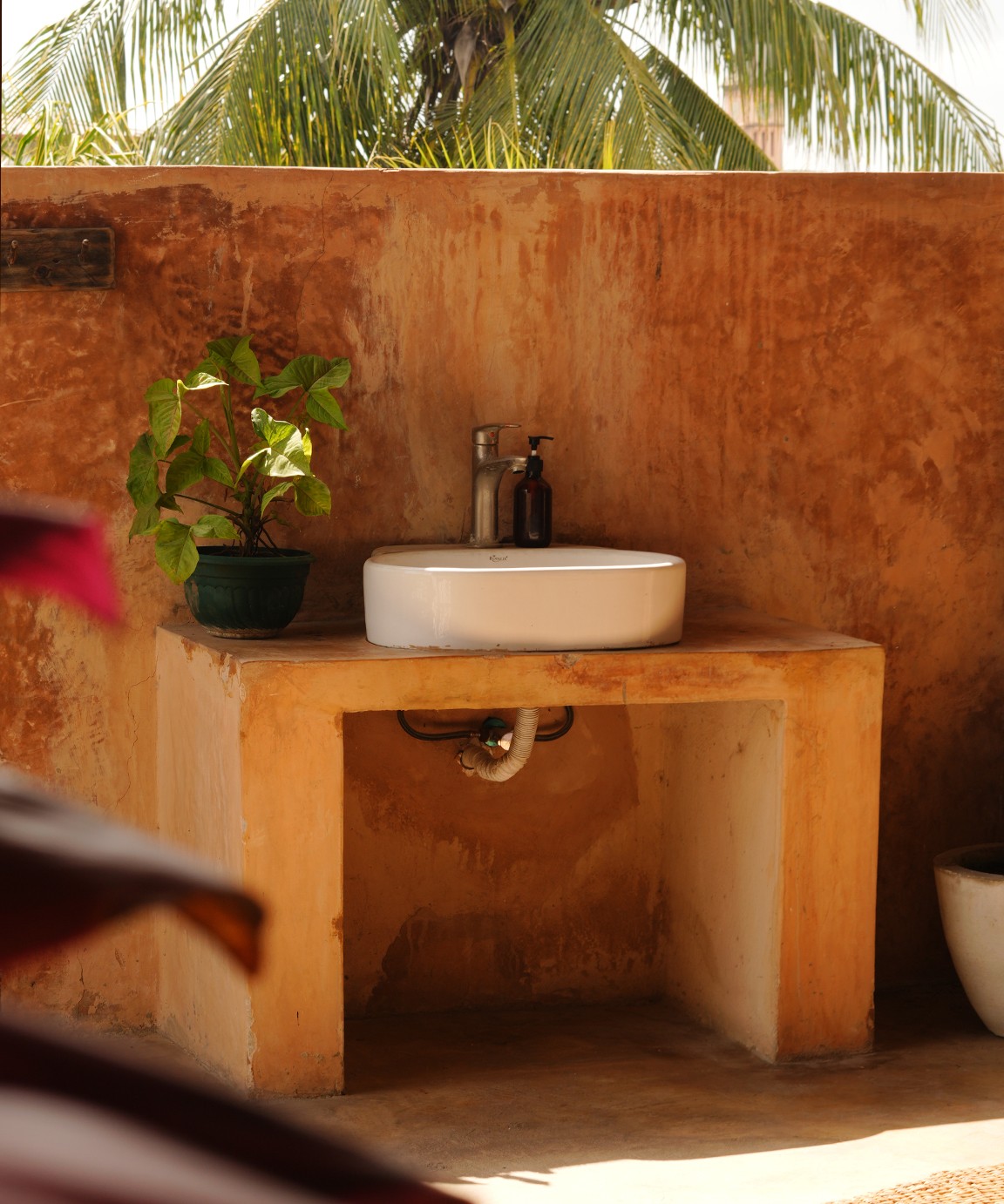 An open-air basin set into a plastered counter beneath palms