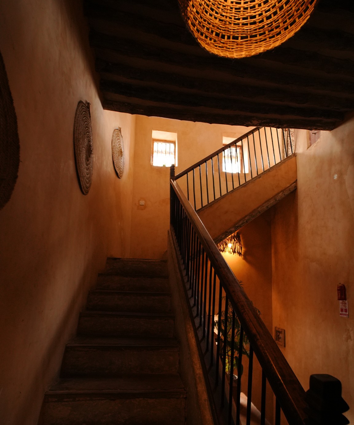 Stairwell with woven discs on the wall and a wicker pendant overhead